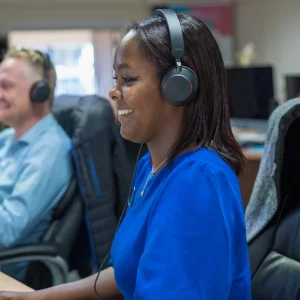 Image of a person smiling with a headset on at a desk